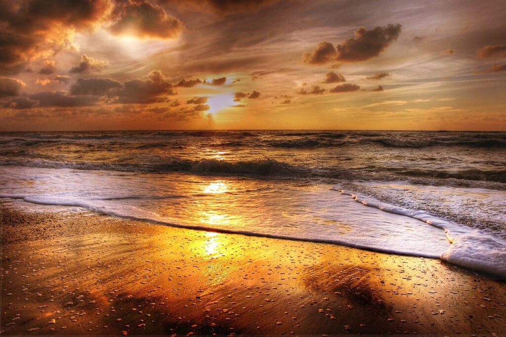 Ein goldener Sonnenuntergang am Meer, bei dem die Wellen sanft an den Strand auslaufen.
