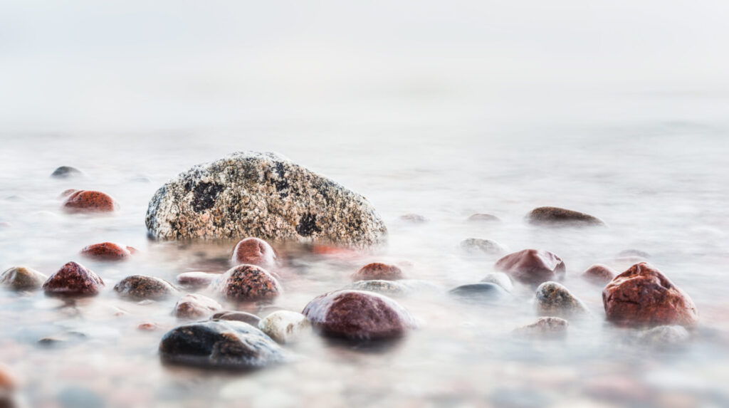 Von sanftem, klarem Wasser umspülte Mineralsteine, die Reinheit und Natürlichkeit symbolisieren.