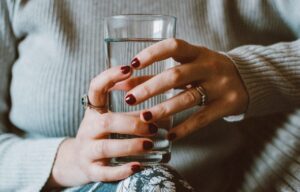 Eine Frau in gemütlicher Kleidung hält ein Glas mit frischem, klarem Wasser in beiden Händen.