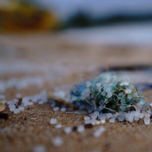 Nahaufnahme von einem alten Fischernetz und Mikroplastik-Granulat, angespült an einem Sandstrand.