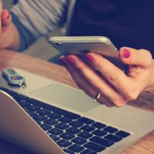 Eine Person greift während der Arbeit am Laptop zur ungesunden Gewohnheit, das Smartphone zu nutzen.