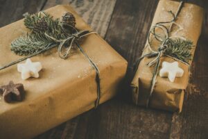 Zwei liebevoll in Packpapier verpackte Weihnachtsgeschenke, dekoriert mit Tannenzweigen und Plätzchen auf einem Holztisch.