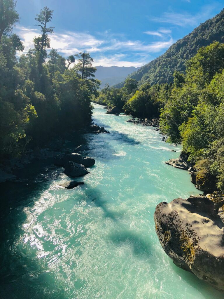 Ein wilder, türkisfarbener Fluss, umgeben von dichten Wäldern und Bergen, symbolisiert die Reinheit und Natürlichkeit von Wasser.