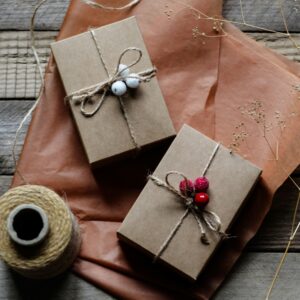 Zwei in naturbraunes Papier verpackte Geschenke, dekoriert mit Beeren und Schnur, liegen auf einem rustikalen Holztisch.