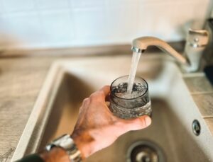Eine Person füllt ein Glas mit frischem, klarem Wasser direkt aus dem Küchenwasserhahn.