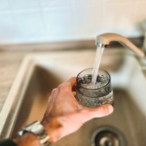 Eine Person füllt ein Glas mit frischem, klarem Wasser direkt aus dem Küchenwasserhahn.