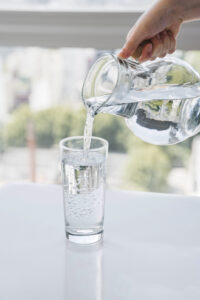 Eine Hand gießt klares, gefiltertes Wasser aus einer Glaskaraffe in ein Trinkglas.